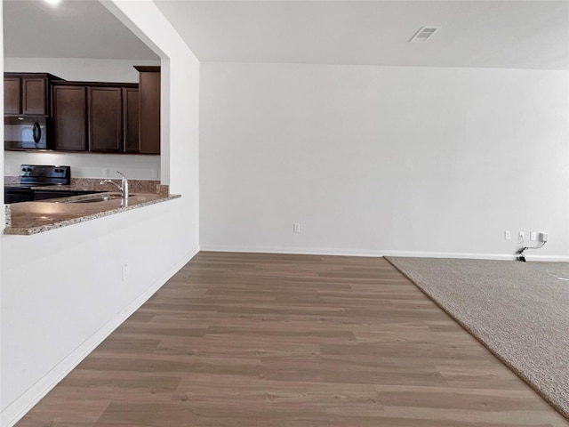 kitchen with light stone counters, dark brown cabinets, sink, black appliances, and hardwood / wood-style floors