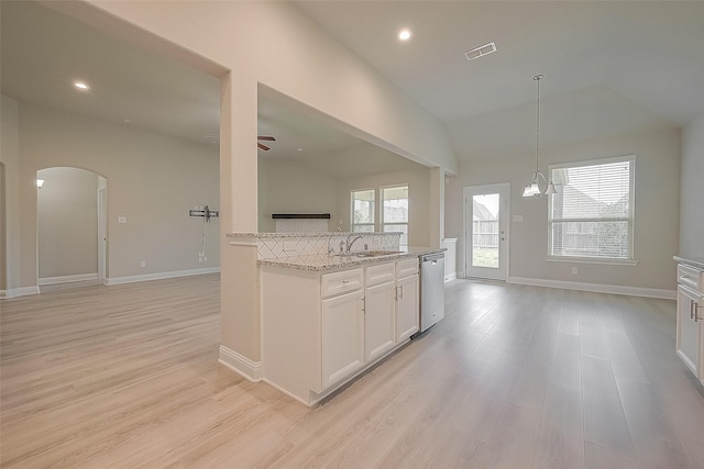 kitchen with light wood-type flooring, stainless steel dishwasher, light stone counters, vaulted ceiling, and white cabinets