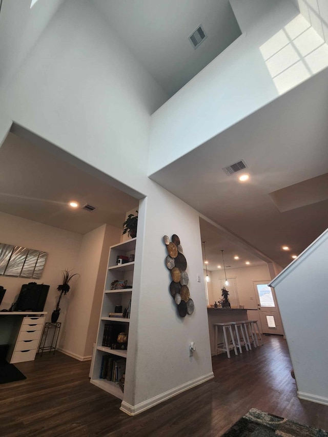 hallway featuring a towering ceiling and dark wood-type flooring