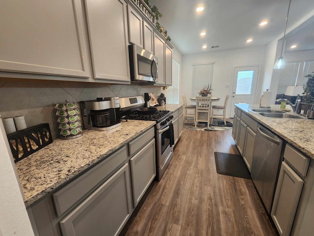 kitchen featuring sink, hanging light fixtures, light stone counters, dark hardwood / wood-style flooring, and appliances with stainless steel finishes