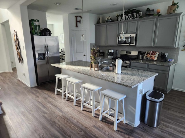 kitchen with a kitchen island with sink, a kitchen breakfast bar, gray cabinets, appliances with stainless steel finishes, and dark hardwood / wood-style flooring