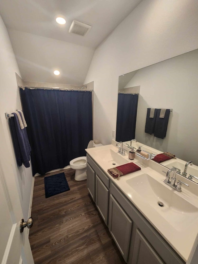 bathroom featuring wood-type flooring, vanity, toilet, and lofted ceiling