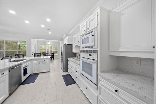 kitchen with appliances with stainless steel finishes, tasteful backsplash, light stone counters, sink, and white cabinetry