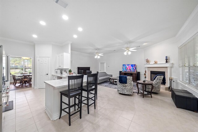 kitchen with white cabinetry, ornamental molding, ceiling fan, light tile patterned floors, and a kitchen breakfast bar