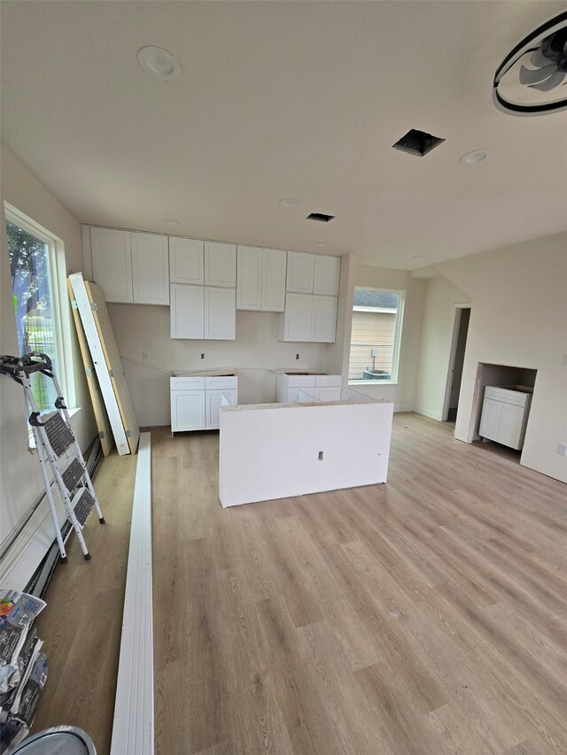 kitchen with white cabinets, a center island, and light wood-type flooring