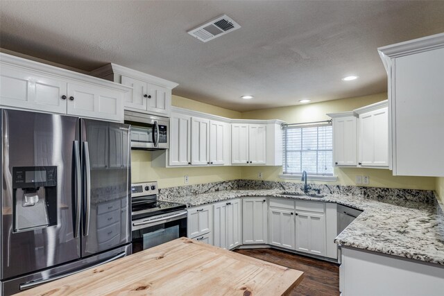 kitchen with appliances with stainless steel finishes, light stone counters, dark wood-type flooring, sink, and white cabinets