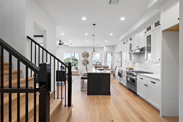 kitchen with light wood-type flooring, white cabinetry, an island with sink, and appliances with stainless steel finishes