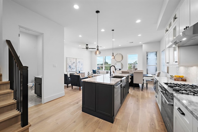 kitchen featuring light wood-type flooring, stainless steel appliances, a kitchen island with sink, white cabinetry, and hanging light fixtures