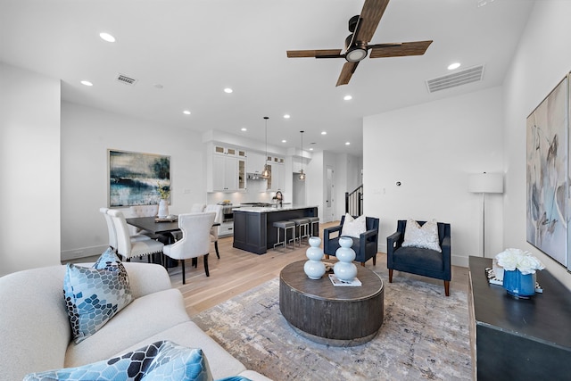 living room featuring ceiling fan, sink, and light wood-type flooring