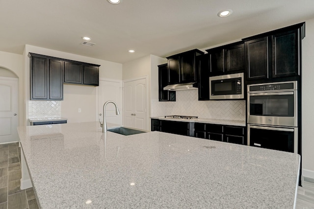 kitchen featuring a center island with sink, light stone counters, sink, and appliances with stainless steel finishes