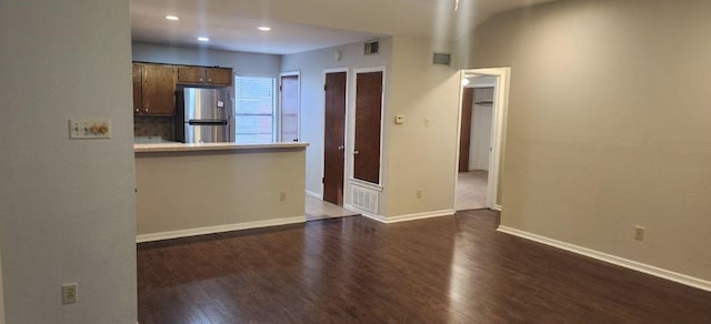 kitchen featuring kitchen peninsula, decorative backsplash, dark hardwood / wood-style flooring, and stainless steel refrigerator