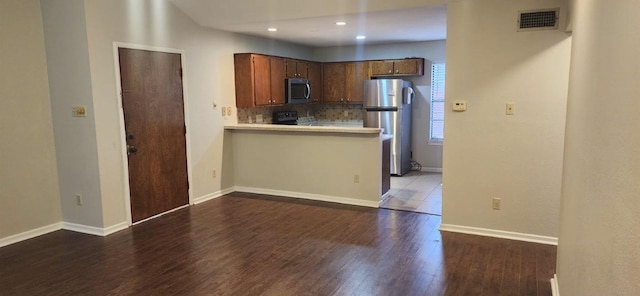 kitchen featuring backsplash, kitchen peninsula, dark hardwood / wood-style floors, and appliances with stainless steel finishes