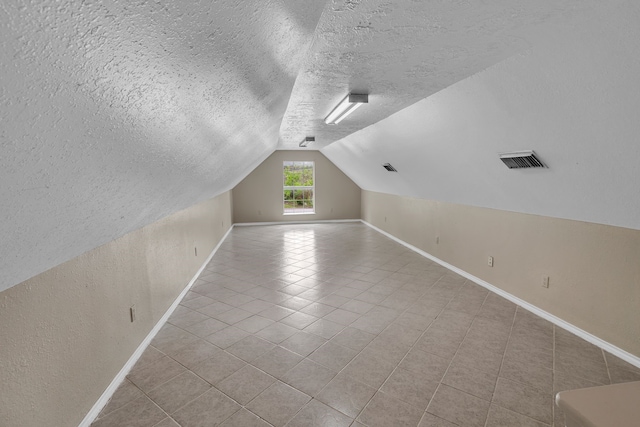 additional living space featuring lofted ceiling, light tile patterned floors, and a textured ceiling