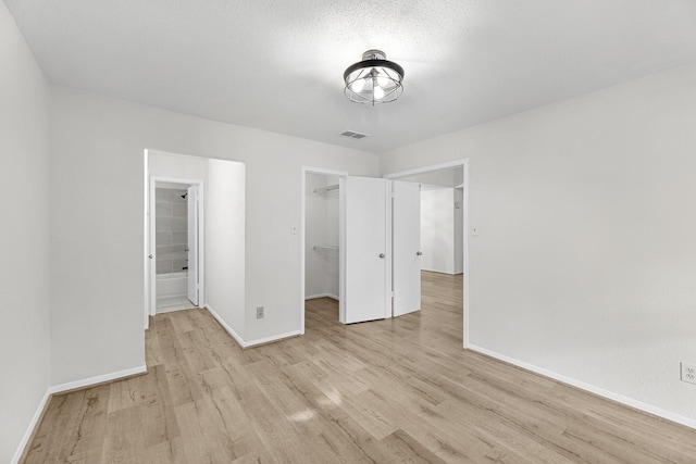 unfurnished bedroom featuring a textured ceiling, a walk in closet, light hardwood / wood-style floors, and a closet