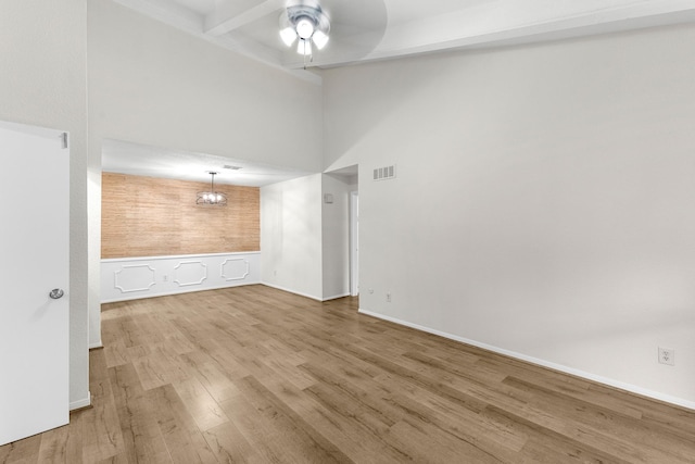 empty room featuring hardwood / wood-style flooring, ceiling fan, a towering ceiling, and beamed ceiling