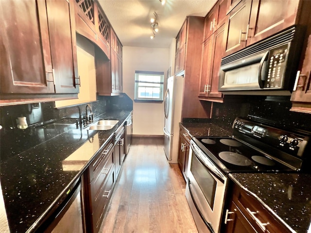 kitchen with dark stone counters, stainless steel appliances, light hardwood / wood-style floors, and sink