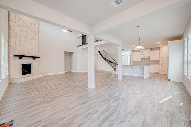 unfurnished living room featuring a stone fireplace, ceiling fan, and light hardwood / wood-style flooring