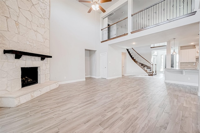 unfurnished living room with ceiling fan, light hardwood / wood-style floors, a stone fireplace, and a high ceiling