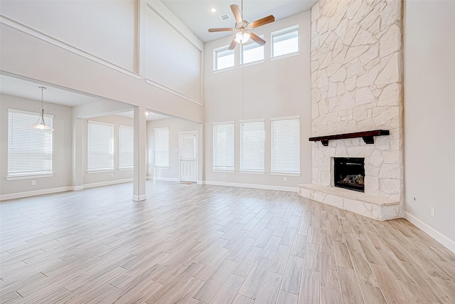 unfurnished living room featuring a towering ceiling, a stone fireplace, and ceiling fan