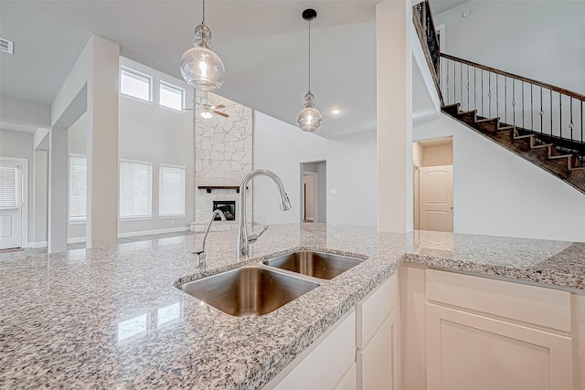 kitchen featuring pendant lighting, sink, light stone countertops, a fireplace, and white cabinetry