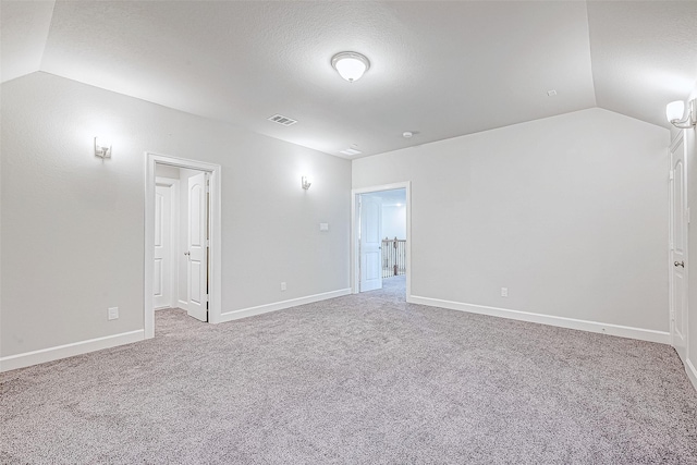 carpeted spare room with a textured ceiling and lofted ceiling