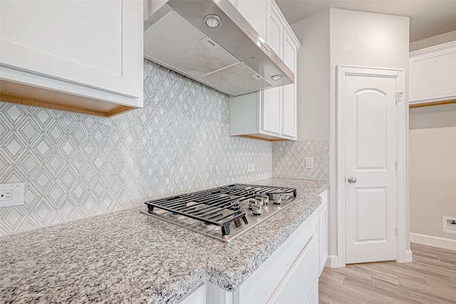 kitchen with white cabinets, wall chimney range hood, light hardwood / wood-style flooring, light stone countertops, and stainless steel gas cooktop