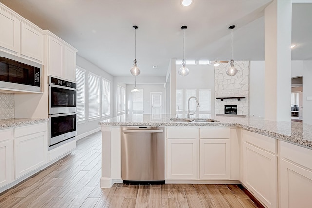 kitchen with appliances with stainless steel finishes, a fireplace, sink, light hardwood / wood-style flooring, and white cabinets