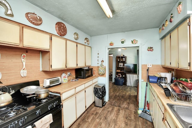 kitchen with cream cabinets, a textured ceiling, dark wood-type flooring, and black appliances