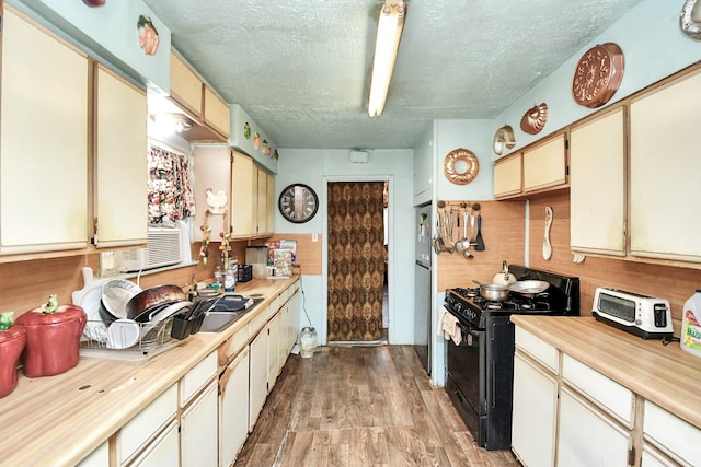 kitchen with stainless steel fridge, black gas range, a textured ceiling, and light hardwood / wood-style floors