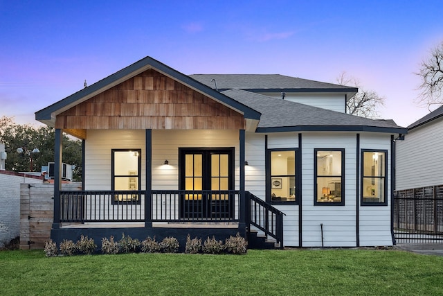 back house at dusk featuring a lawn and a porch