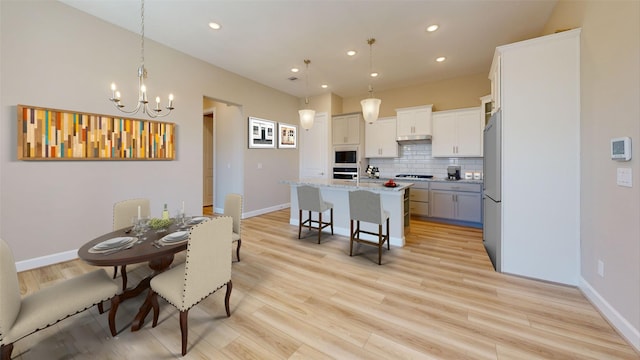 kitchen with decorative light fixtures, light hardwood / wood-style floors, light stone countertops, and an island with sink