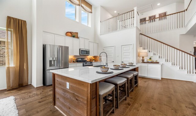 kitchen with stainless steel appliances, a kitchen island with sink, dark wood-type flooring, white cabinets, and a high ceiling