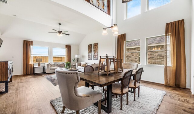 dining room featuring wood-type flooring, ceiling fan with notable chandelier, and high vaulted ceiling