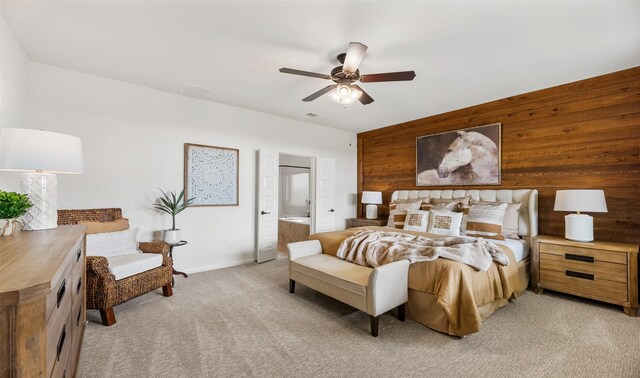 bedroom with ceiling fan, light carpet, wooden walls, and ensuite bath