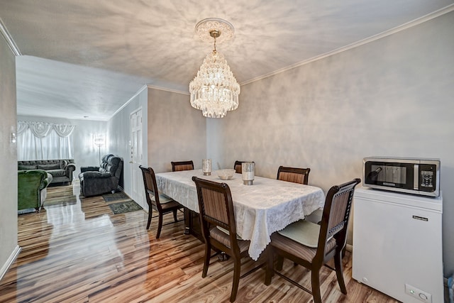 dining room with light wood-type flooring, an inviting chandelier, and ornamental molding