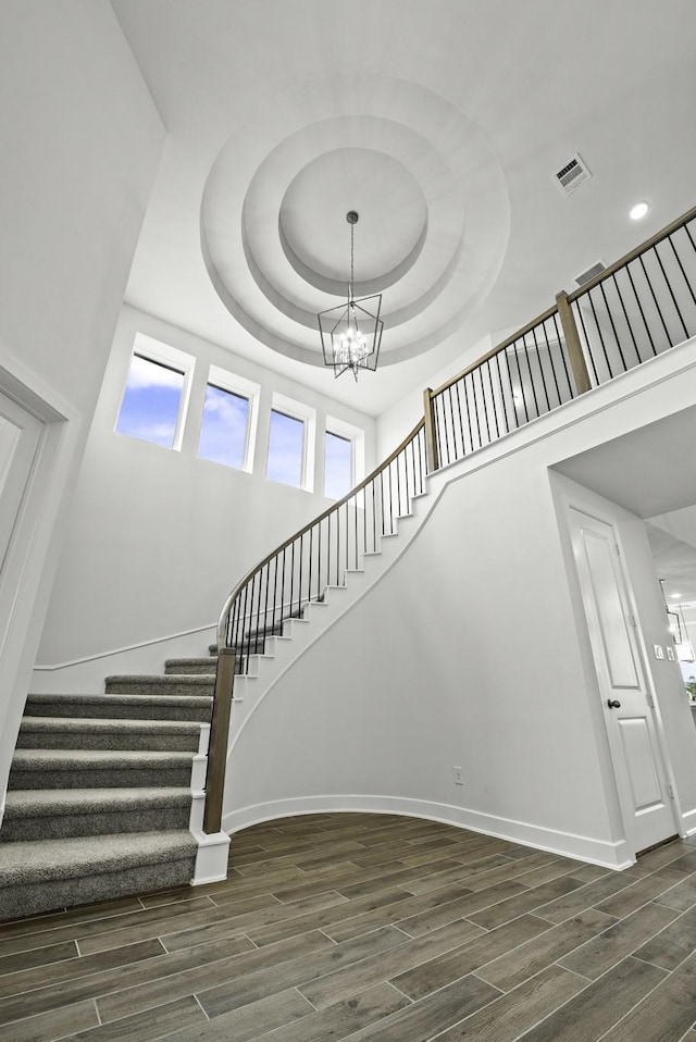 stairs with a tray ceiling, wood-type flooring, and an inviting chandelier