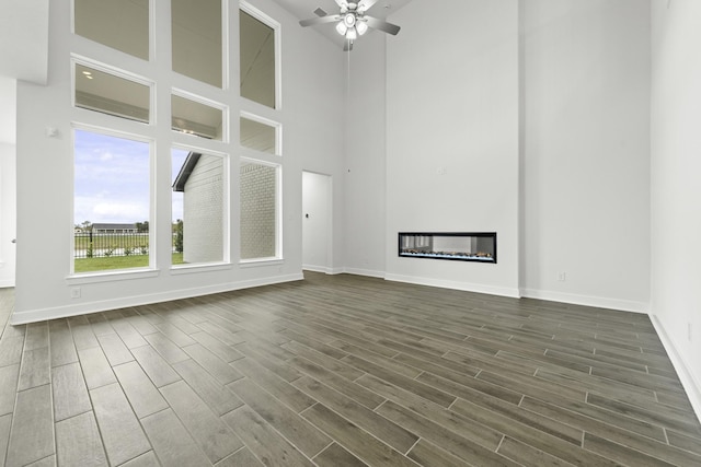 unfurnished living room featuring a high ceiling, ceiling fan, and dark wood-type flooring