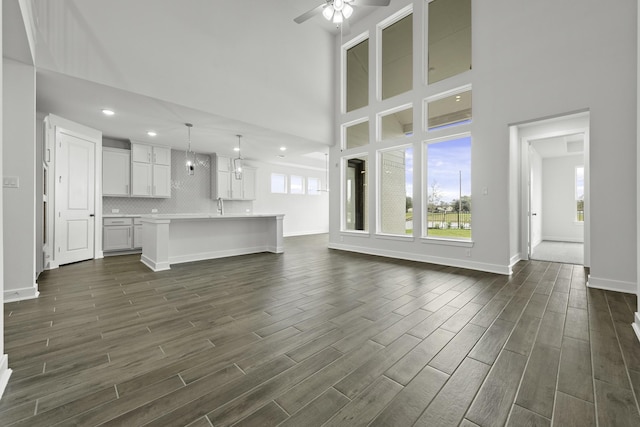 unfurnished living room with ceiling fan, dark hardwood / wood-style flooring, a high ceiling, and sink