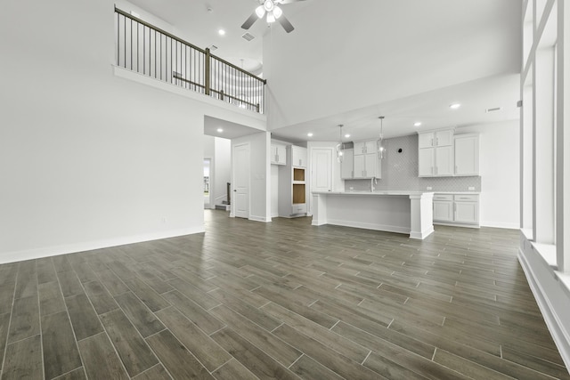 unfurnished living room with a towering ceiling, ceiling fan, and dark wood-type flooring