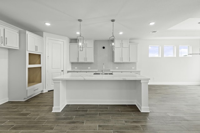 kitchen with light stone counters, sink, decorative light fixtures, a center island with sink, and white cabinetry