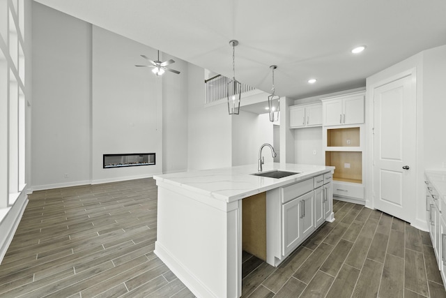 kitchen with light stone counters, sink, a center island with sink, white cabinets, and dark hardwood / wood-style floors