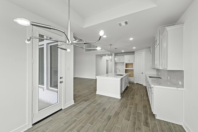 kitchen featuring dark hardwood / wood-style flooring, white cabinetry, a center island with sink, and sink