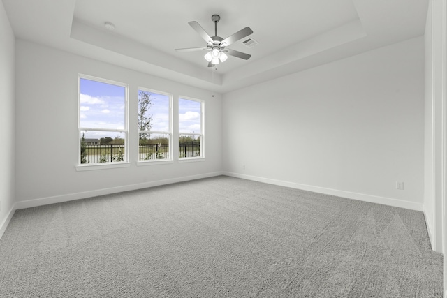 carpeted spare room featuring a raised ceiling and ceiling fan