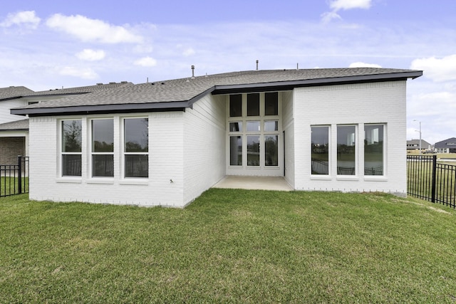 rear view of house featuring a yard, brick siding, a shingled roof, and fence