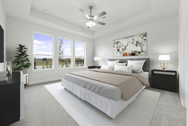 carpeted bedroom with ceiling fan and a tray ceiling