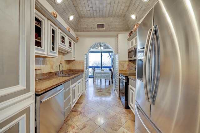 kitchen with sink, stainless steel appliances, tasteful backsplash, brick ceiling, and white cabinets