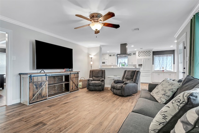 living room featuring light wood-type flooring, ceiling fan, ornamental molding, and sink