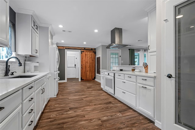 kitchen featuring a barn door, decorative backsplash, island exhaust hood, white appliances, and white cabinetry