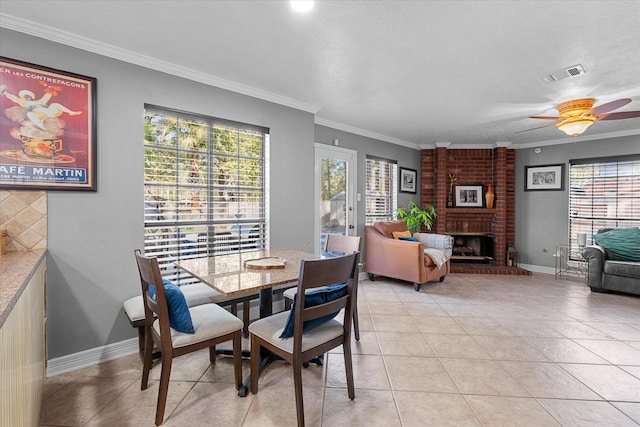 tiled dining area with a brick fireplace, ceiling fan, and ornamental molding