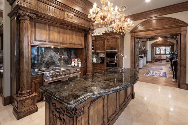 kitchen with an island with sink, appliances with stainless steel finishes, and decorative columns